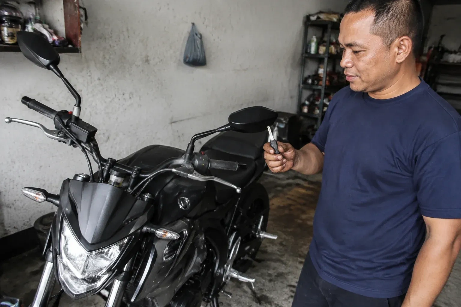 Person holding a key beside a black motorcycle in a garage. — Motorcycle & Scooter Keys, King