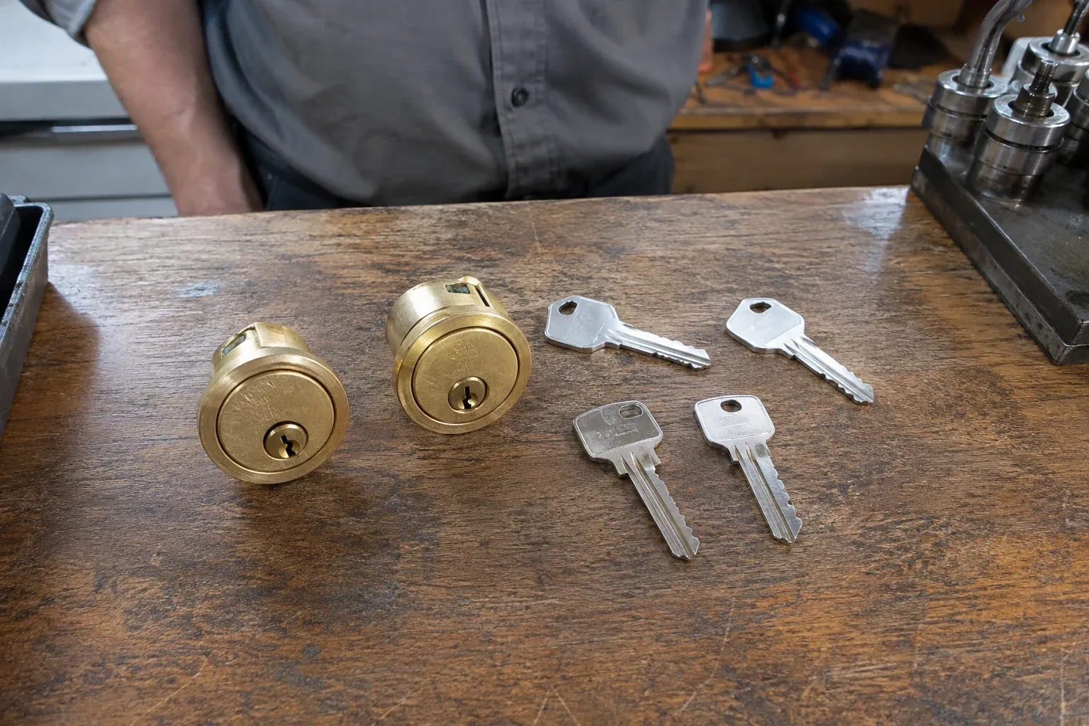Two detached brass lock cylinders and four house keys on a wooden counter. — Lock Rekeying, King