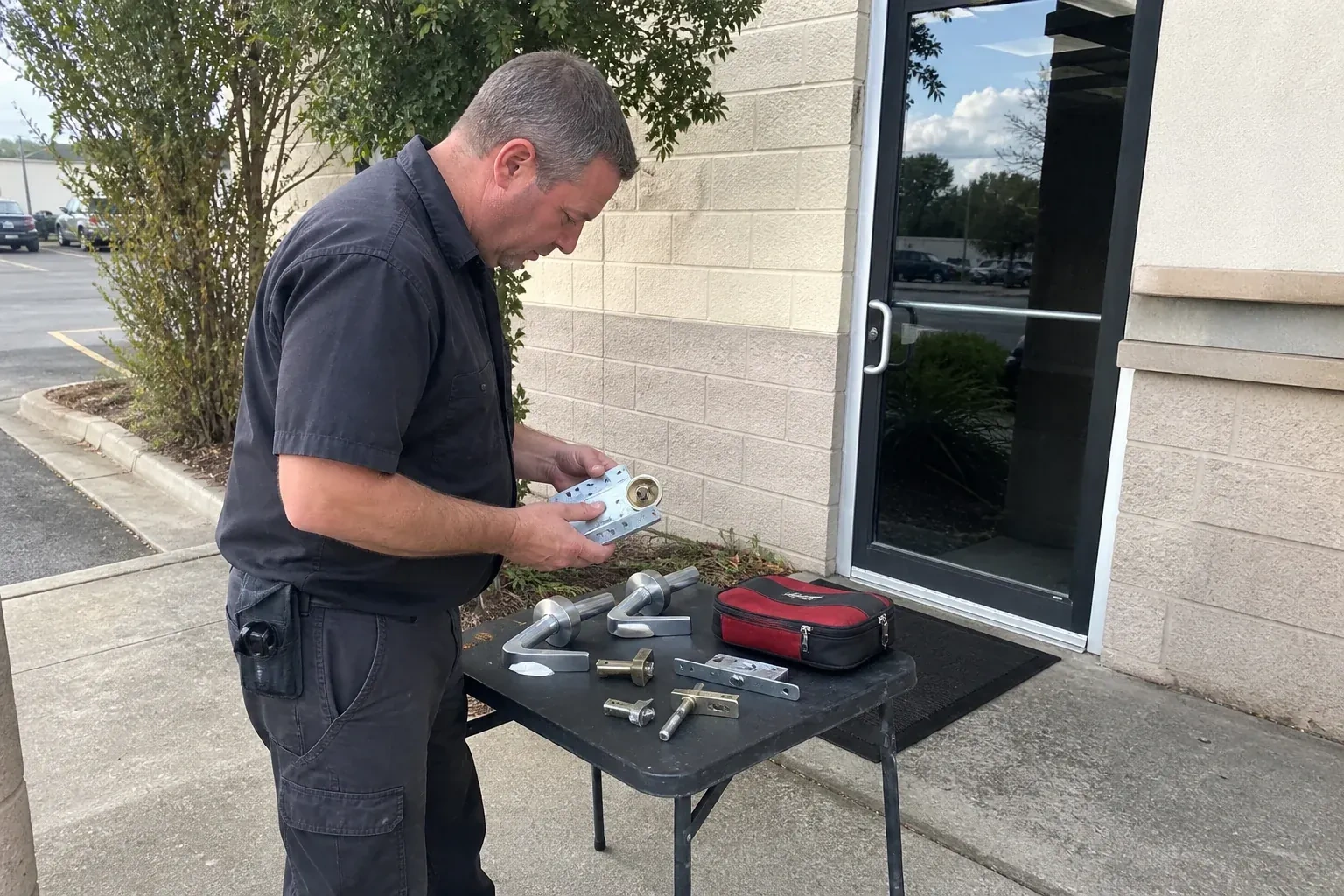 Technician examining detached commercial lock hardware on a table outside a shop entrance. — Business Lockout Service, King